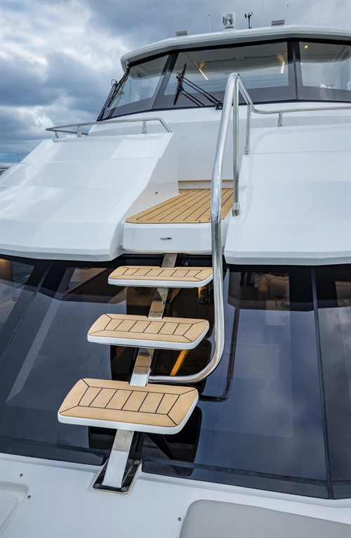 Stainless steel steps with wooden treads leading up to a yacht's upper deck under cloudy skies.